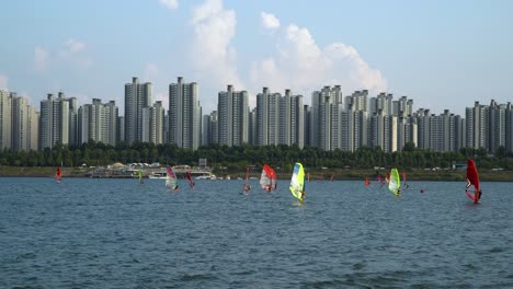 Many-People-Windsurfing-on-Han-River-Daytime,-Jamsil-apartments-on-background,-cloudy-day