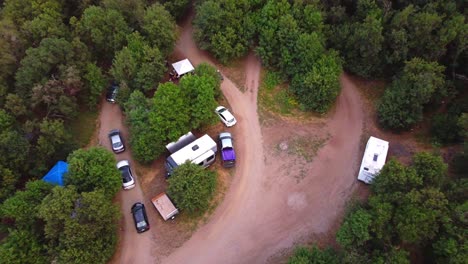 Drone-flying-over-outdoor-nature-wilderness-national-forest-campsite-camp-grounds-with-cars-and-campers-and-ATV-quad-4-wheeler-driving-down-dirt-trail-as-camera-follows-in-to-whip-out