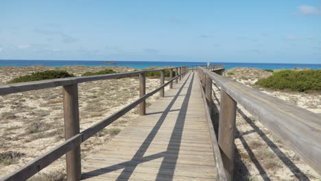 Man-tourist-walking-alone-at-the-end-of-a-long-wooden-bridge-that-goes-towards-the-sea,-sunny-day