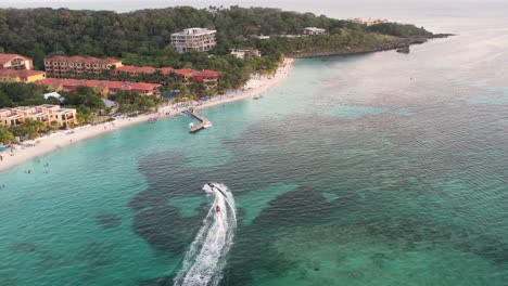 Aerial-view-of-the-coast,-speed-boats,-green-palms-on-sandy-beach-at-sunset