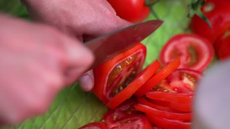 Ripe-fresh-red-tomato-being-sliced-and-cut-with-dull-knife-close-up-camera-shot-during-back-yard-barbecue-party-camp-out-on-green-table,-close-up-shot-slowed-halfway-from-60fps