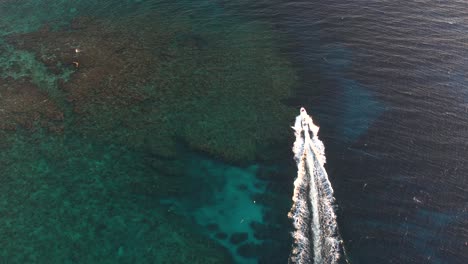 White-speed-boat-moving-on-clear-turquoise-sea-surface-with-coral-reef-towards-an-island