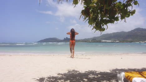 Latin-Girl-in-Bikini-on-Hot-White-Sandy-Beach-Walks-to-Swim-in-Sea,-Gentle-Zoom-in
