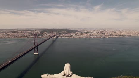 Aerial-dolly-out-shot-of-the-rear-view-of-Catholic-statue-Christ-the-King-at-Almada-overlooking-Lisbon