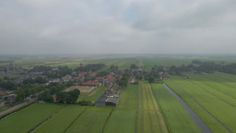 Aerial-of-a-beautiful-Dutch,-rural-town-with-a-spinning-scaffolding-windmill
