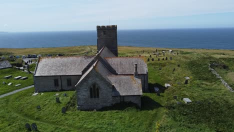 St-Materiana's-church-in-Tintagel-Cornwall-overlooking-the-sunny-sea-side-and-cliffs-in-the-middle-of-the-day-in-summer,-the-shot-I-used-is-a-tripod-shot-with-a-drone-and-it-was-shot-in-1080p-FHD