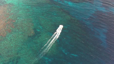 White-speed-boat-on-clear-turquoise-sea-surface-with-coral-reef-towards-an-island