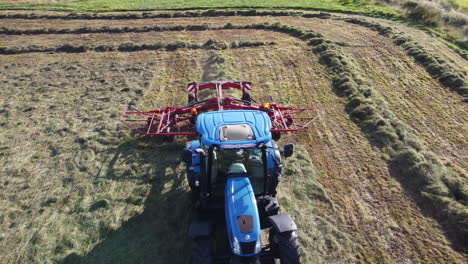 Aerial-flyover-follow-shot-of-a-tractor-collecting-hay-in-a-row