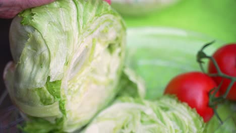 Head-of-fresh-green-lettuce-veggies-being-sliced-chopped-up-with-fresh-red-tomatoes-in-background-of-close-up-shot-during-barbecue-backyard-party,-close-up-shot-slowed-halfway-from-60fps