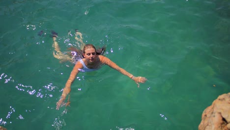 Mujer-En-Bikini-Nadando-Cerca-De-La-Costa-Rocosa-Y-El-Mar-De-Cristal