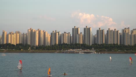 Unrecognizable-People-Windsurfing-on-Han-River-in-Seoul-at-stunning-picturesque-sunset-over-Jamsil-high-storied-apartment-complex
