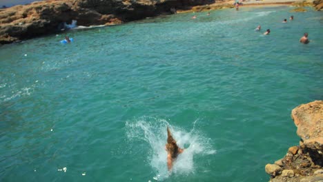 Slow-Motion-Of-A-Female-Tourist-In-Swimwear-Jumps-From-The-Rocky-Edge-Into-Sea-In-Summer