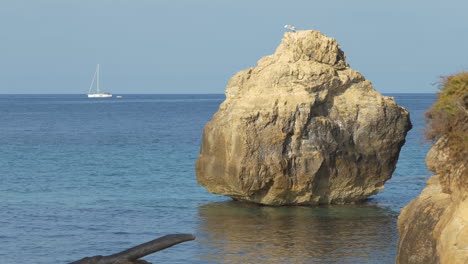 Eiförmiger-Felsen-Im-Mittelmeer-Mit-Einem-Segelboot,-Das-Im-Hintergrund-Auf-Dem-Wasser-Kreuzt