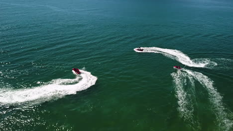 Orbital-shot-of-three-jet-skis-rolling-in-a-blue-and-green-sea