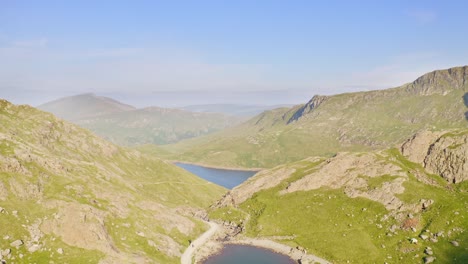 Incredible-crane-up-aerial-reveal-over-Snowdonia-National-Park-in-Wales-with-mountain-ranges-and-lakes-below-on-a-clear-morning