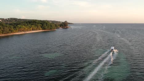Weißes-Schnellboot-Auf-Klarer-Türkisfarbener-Meeresoberfläche-Mit-Korallenriff,-Das-Sich-Auf-Eine-Insel-Zubewegt