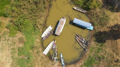 Aerial-revealing-footage-of-a-Boat-Tour-in-Bueng-Boraphet,-Nakhon-Sawan,-Thailand,-a-big-boat-moving-out-of-the-station-pushed-with-a-long-stick-by-a-man