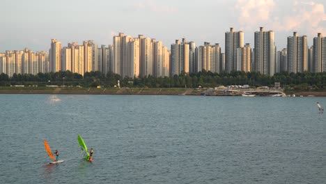 Urban-windsurfing-on-Han-river-in-Jamsil-district-of-Seoul-at-sunset,-Ttuseom-Park-surfing-club,-apartments-on-background