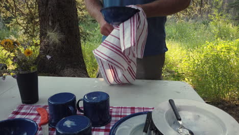 Low-angle-static-shot-of-man-drying-camping-dishes-outdoors-at-campsite