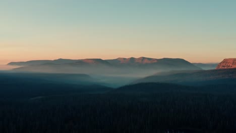 Beautiful-left-trucking-aerial-drone-shot-of-the-stunning-wild-Uinta-Wasatch-Cache-National-Forest-in-Utah-with-large-pine-trees-below-and-stunning-mountains-covered-in-mist-during-a-summer-sunrise