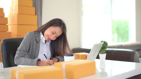 Female-worker-online-store-owner-using-laptop-at-work-preparing-parcel-boxes-checking-eCommerce-shipping-online-retail-e-commerce-store-order-fulfillment-in-dropship-delivery-post-office-from-home