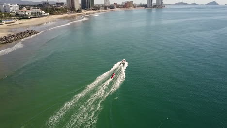 Red-tube-water-sled-pulled-by-a-speeding-boat-near-the-shore,-Mazatlan-Mexico
