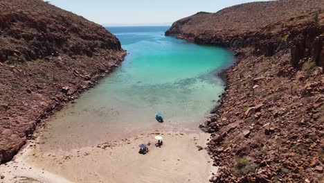Aerial:-small-boat-and-beachgoers-moored-on-deserted-empty-beach,-Espiritu-Santo-Island,-Mexico