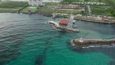 Drone-shot-revealing-with-a-small-orbit-the-entire-background-around-the-wave-breaker,-the-lighthouse,-restaurant-and-the-dock