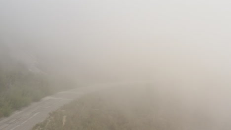 Drone-view-of-windy-road-on-side-of-mountain-vanishing-into-clouds