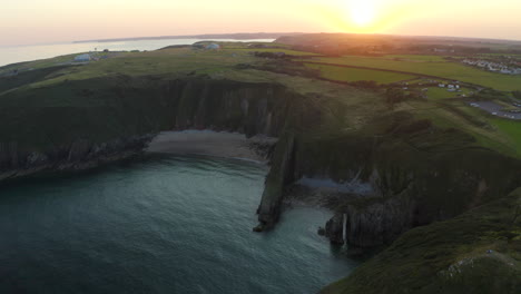 An-aerial-shot-revealing-the-Pembrokeshire-coast-near-Manorbier-beach-with-Church-door-cove-at-sunset-on-a-calm-summer-day