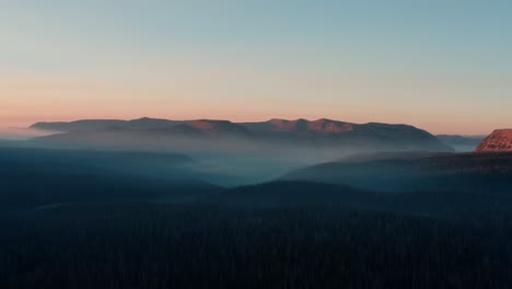 Beautiful-static-aerial-drone-shot-of-the-stunning-wild-Uinta-Wasatch-Cache-National-Forest-in-Utah-with-large-pine-trees-below-and-stunning-mountains-covered-in-mist-during-a-summer-sunrise
