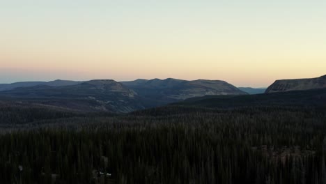 Beautiful-left-trucking-aerial-drone-shot-of-the-stunning-wild-Uinta-Wasatch-Cache-National-Forest-in-Utah-with-trees-below-and-large-pointy-Rocky-Mountains-on-a-misty-summer-morning