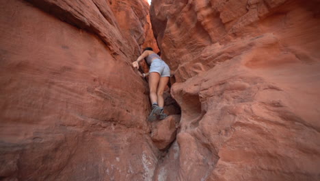 Young-Woman-Climbing-on-a-Red-Rocks-in-Very-Narrow-Eroded-Slot-Canyon,-Valley-of-Fire-State-Park,-Nevada-USA,-Full-Frame