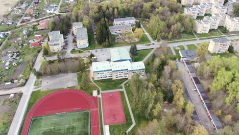 School-building-with-basketball-court-and-football-stadium,-aerial-orbit-view