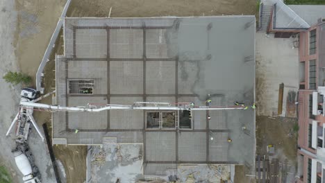 Top-View-Of-Construction-Men-At-Work-Pouring-And-Spreading-Concrete-Mix-On-Slab-Floor-Of-A-Building-With-Installed-Rebars