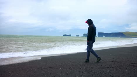 Hombre-Caminando-Solo-En-La-Famosa-Playa-De-Arena-Negra-De-Reynisfjara-En-El-Sur-De-Islandia