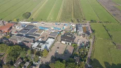 Aerial-of-industrial-buildings-with-solar-panels-on-rooftop-at-the-edge-of-green-meadows