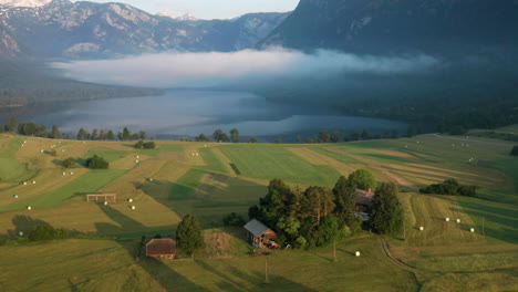 Wolken-Und-Nebel-über-Dem-Bohinjer-See-Von-Landschaftsfeldern-Mit-Heuballen-Bei-Sonnenaufgang-In-Slowenien