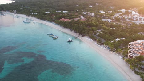 Cinematic-Aerial-view-of-Caribbean-reef-with-boats,-turquoise-water,-beach,-resorts-at-sunrise,-island-background,-Roatan-island,-Honduras,-Central-America