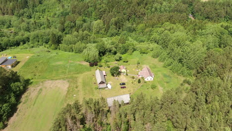Small-homestead-surrounded-by-dense-forest-in-Lithuania,-aerial-orbit-timelpase-view