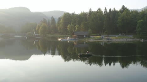 Fischer-Auf-Dem-Boot,-Das-An-Einem-Sonnigen-Tag-Am-Bohinjer-See-Schwimmt,-Mit-Reflexionen-Auf-Ruhigem-Wasser