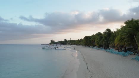 Barcos-Blancos-Sobre-Las-Olas-En-Agua-De-Mar-Azul,-Palmeras-Y-Resorts-En-La-Costa-Caribeña