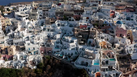 Oia-City-With-White-And-Blue-Houses-In-Santorini,-Greece---aerial-drone-shot