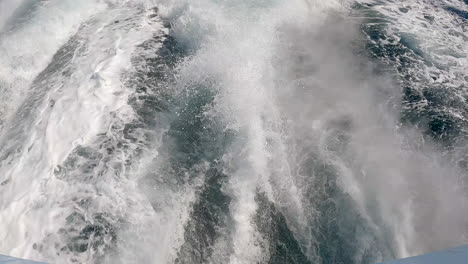 White-water-sea-foam-in-the-wake-of-a-motorboat-on-the-ocean-water---tilt-up-reveal-of-the-pacific-horizon-in-slow-motion