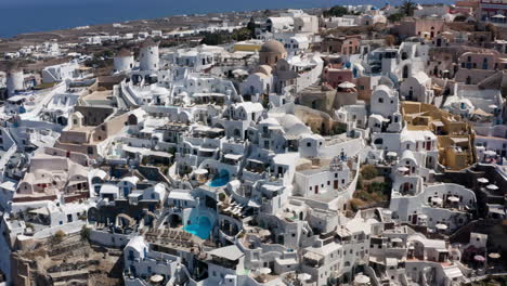 Traditional-White-Buildings-On-The-Oia-Village-And-The-Sea,-Santorini-Island,-Greece---aerial-pullback