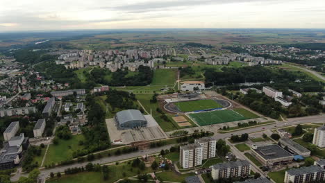 Football-field-and-old-block-apartment-buildings-in-cityscape-of-Jonava,-aerial-drone-view