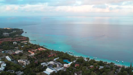 Cinematic-Aerial-view-of-Caribbean-coast-with-boats,-turquoise-water,-beach,-resorts-during-sunrise,-island-background,-Roatan-island,west-end,-Honduras