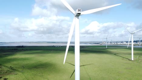 Aerial-view-flying-around-renewable-energy-wind-farm-wind-turbines-spinning-on-British-countryside-rising-right