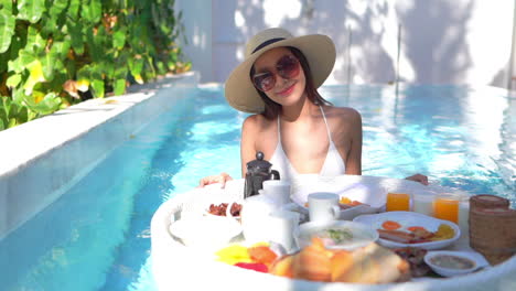 Pretty-Exotic-Woman-With-Breakfast-Plate-for-Two-in-Swimming-Pool-on-Sunny-Morning-at-Tropical-Holiday,-Full-Frame