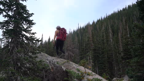 Female-Hiker-With-Backpack-and-Photo-Camera-Climbing-on-Rock-in-Conifer-Forest